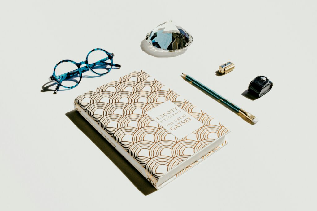 An image featuring 'The Great Gatsby' book with stylish glasses, a crystal, pencil, sharpener, and ring laid out neatly on a white background . Scrapbook Kits