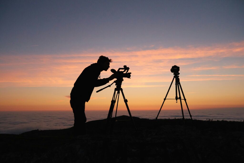 Silhouette of a videographer filming with a camera on tripod during sunset on a mountain